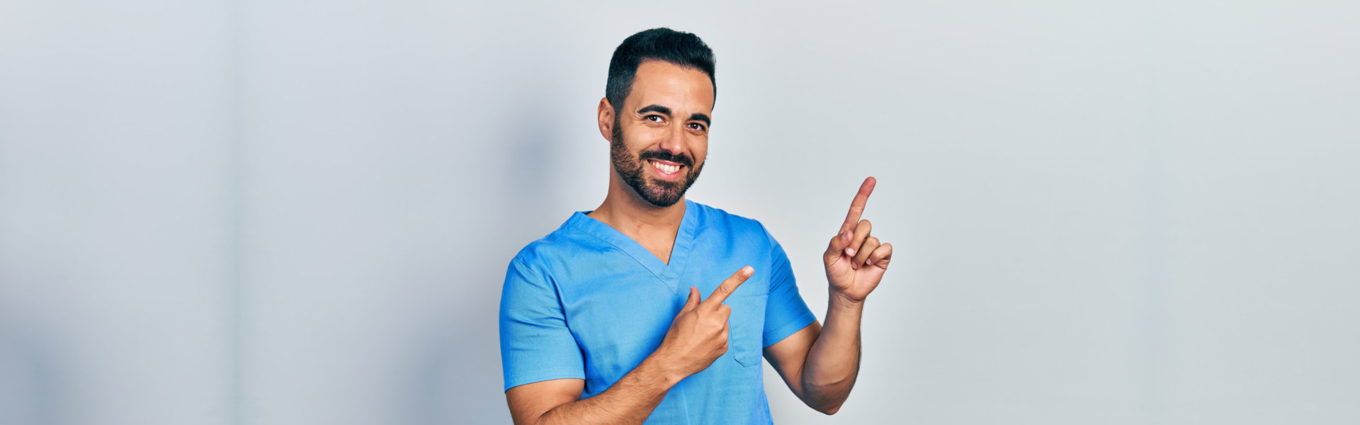 Handsome hispanic man with beard wearing blue male nurse uniform smiling and looking at the camera
